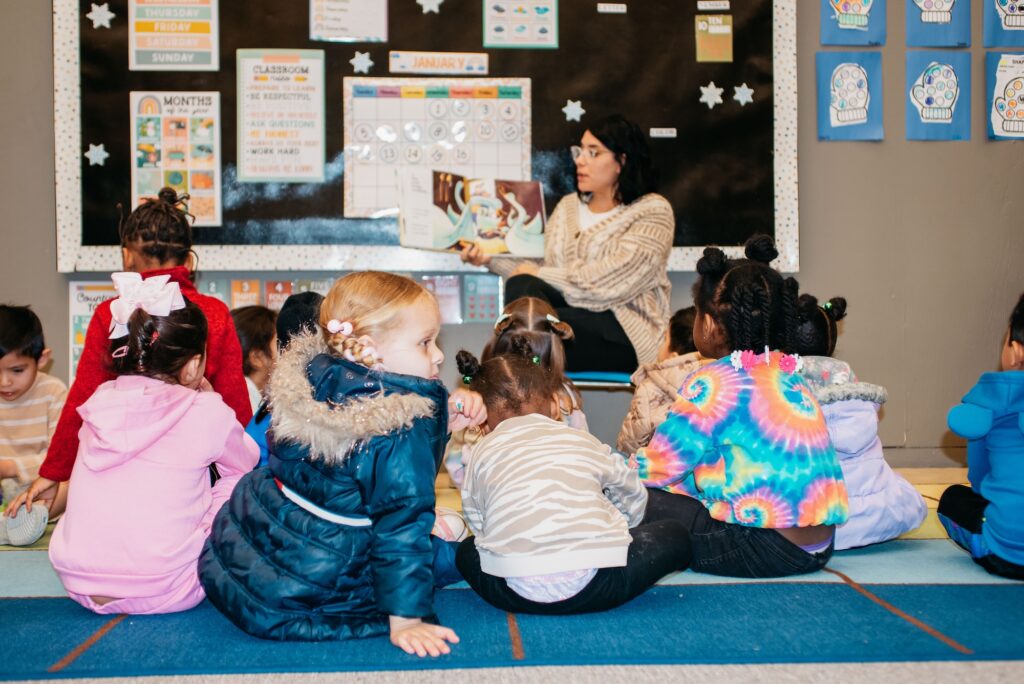 A woman reads a story to a group of attentive children during a toddler program.