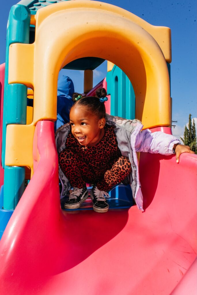 Young girl crouching playfully at the top of a colorful playground slide