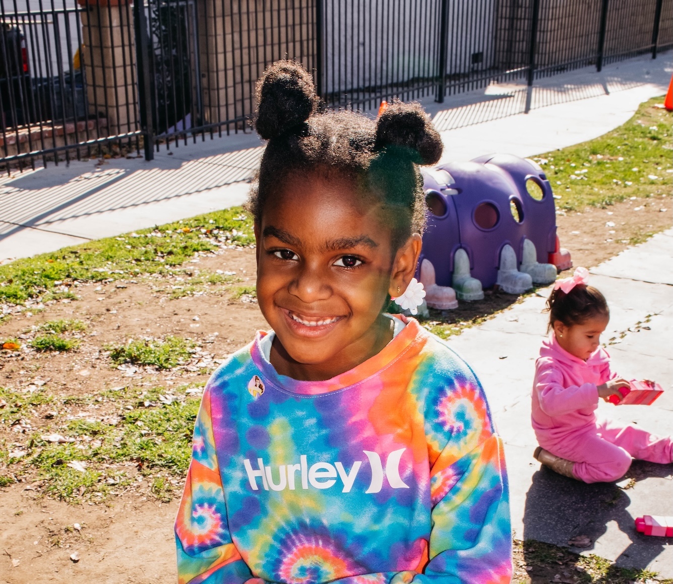 Smiling girl in a colorful tie-dye sweatshirt at a Transitional Pre-K Program.