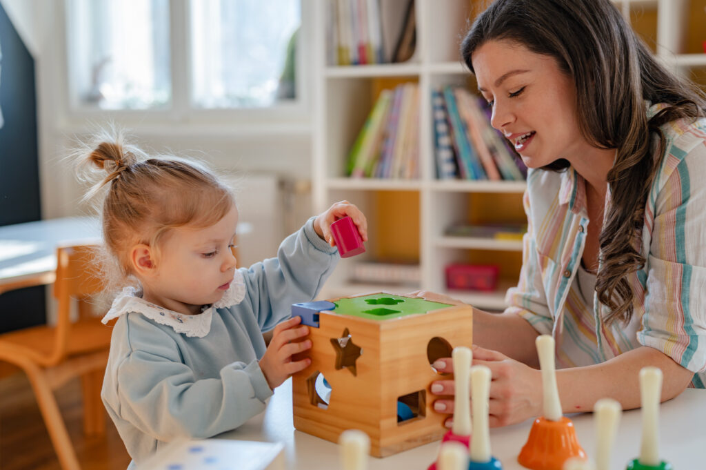 Woman and young girl playing with a shape sorter in a preschool classroom.