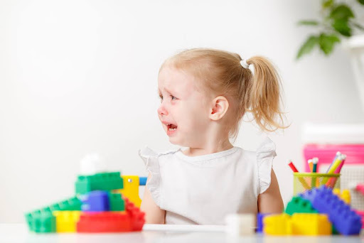 Portrait of crying little girl playing at table.Frustrated girl showing moody behavior and long face